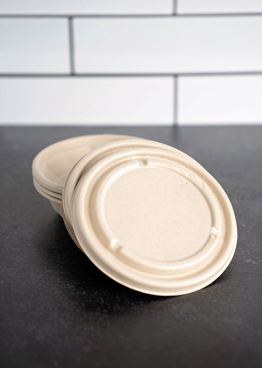 A stack of round, beige biodegradable sugar cane pulp food containers eco-friendly with anti-leak lids